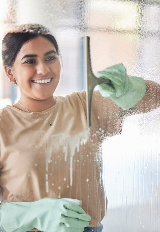Happy, smile and girl cleaning window with spray bottle and soap or detergent, housekeeper in home .