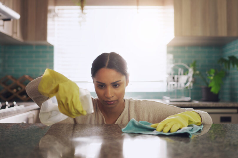 Shot of a young woman scrubbing down her kitchen counter at home.