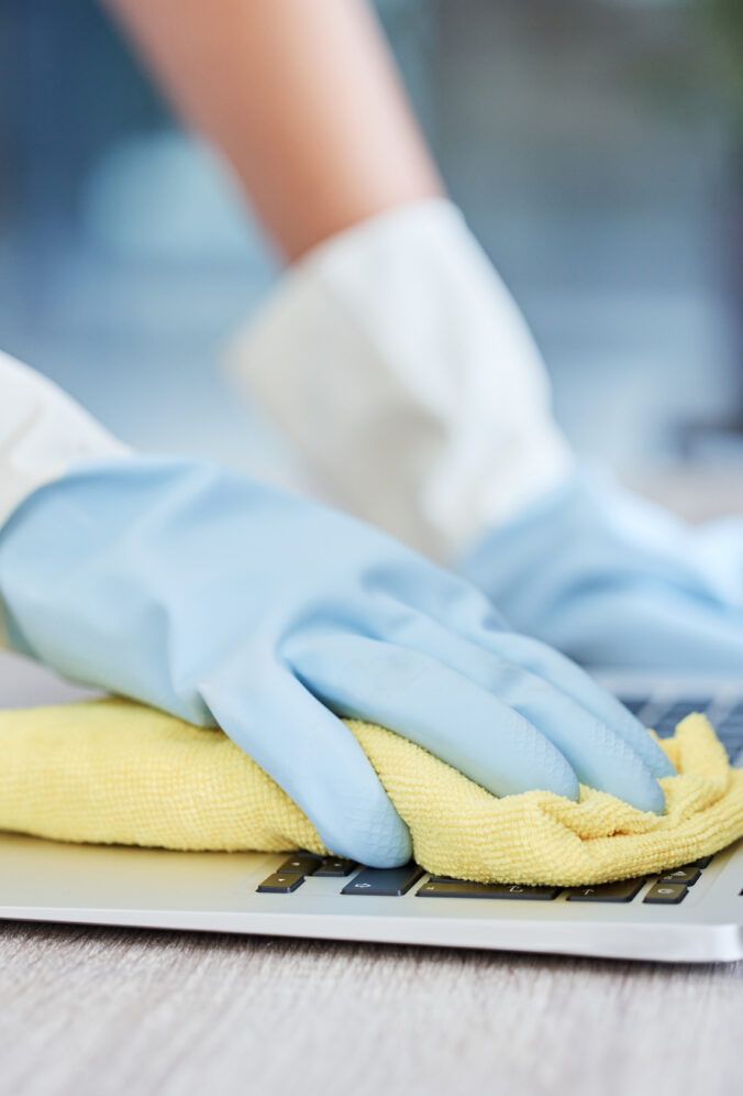 An unrecognizable woman cleaning her laptop in her apartment. One unknown woman using a rag to remo.
